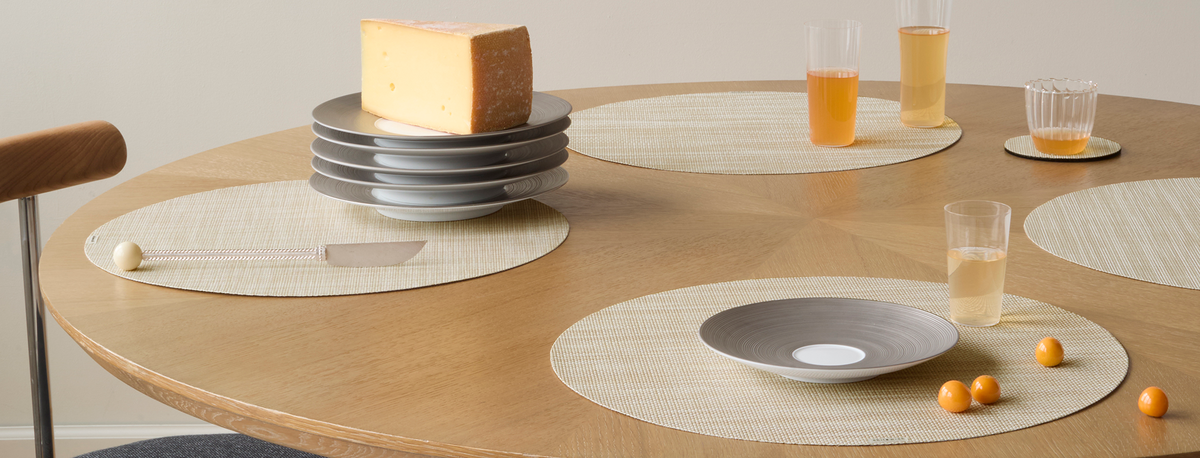 Chilewich woven placemats styled on a warm wood table with gray dishes and amber drinks