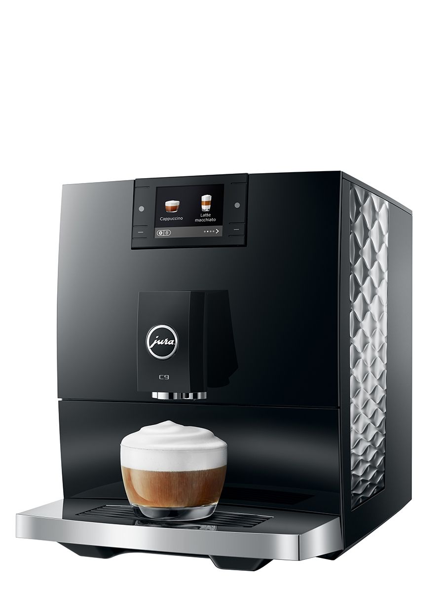 Angled front view of the JURA C9 Piano Black coffee machine preparing a milk-based coffee drink in a glass cup with foam on top.