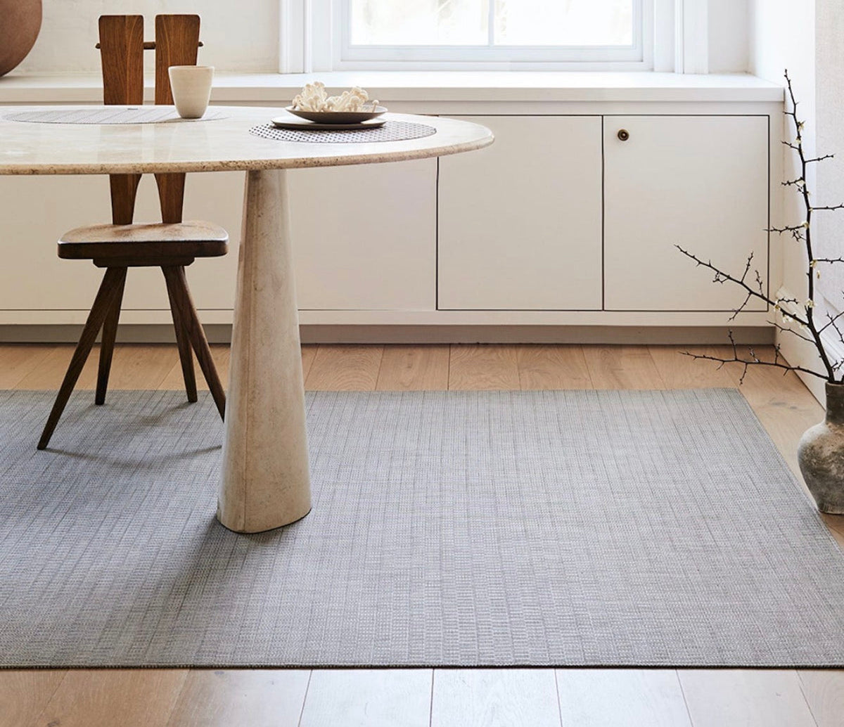 Gray woven Chilewich rug beneath a dining table in a bright neutral room