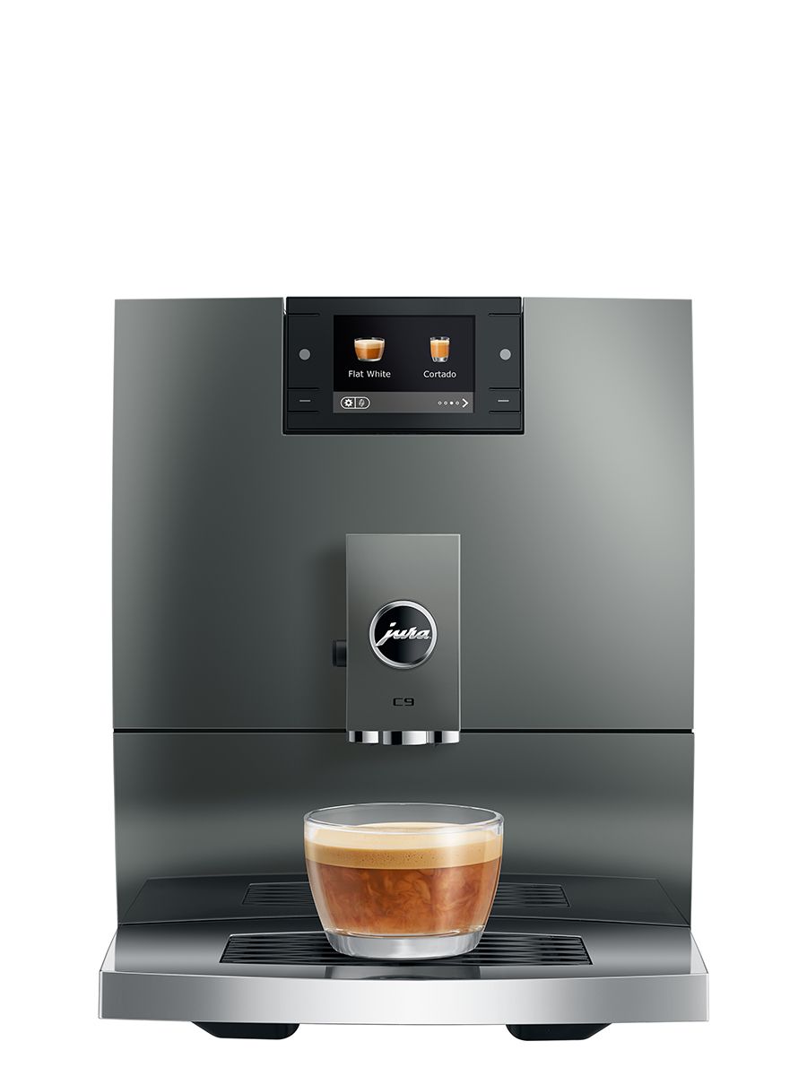 Front view of the JURA C9 Piano Inox automatic coffee machine dispensing a milk-based coffee drink into a glass cup on the drip tray.