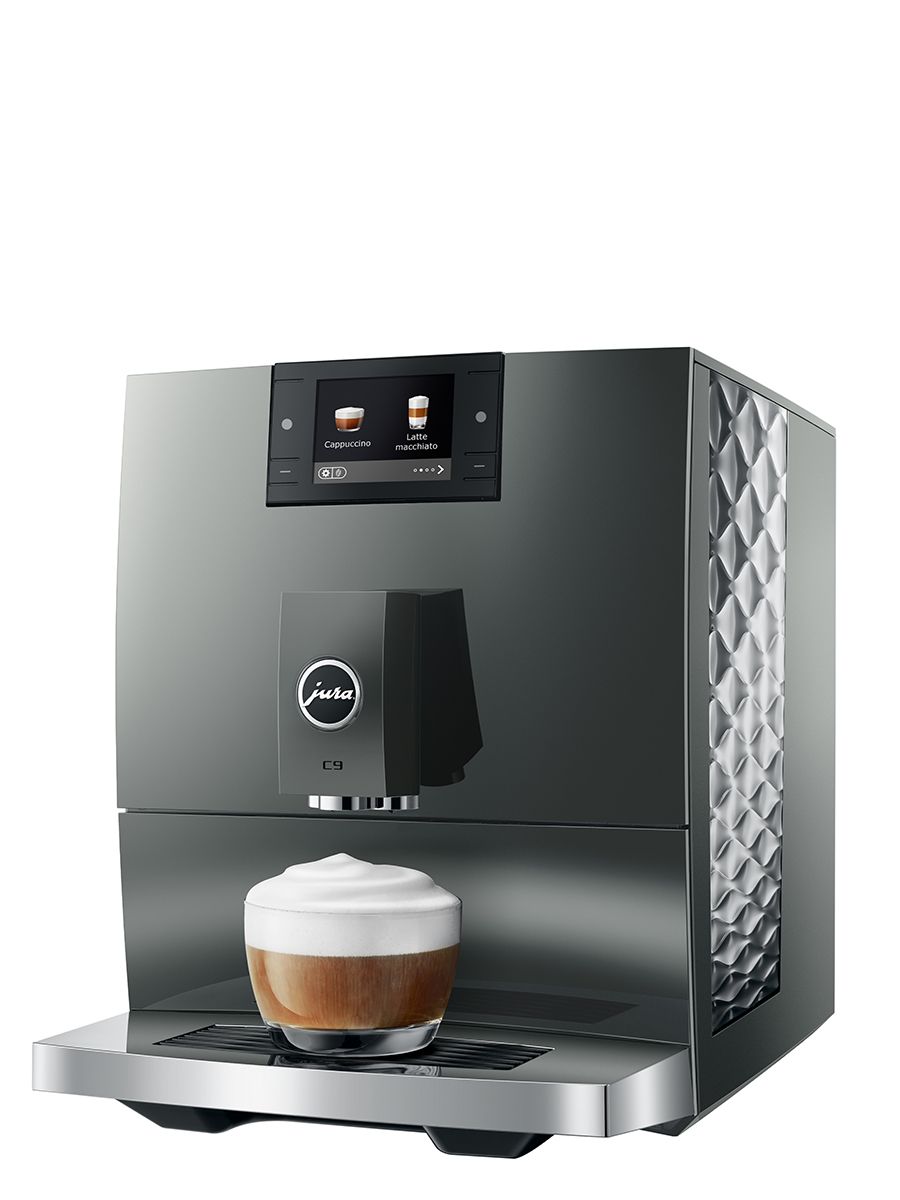 Angled front view of the JURA C9 Piano Inox coffee machine preparing a milk-based coffee drink with foam in a glass cup.