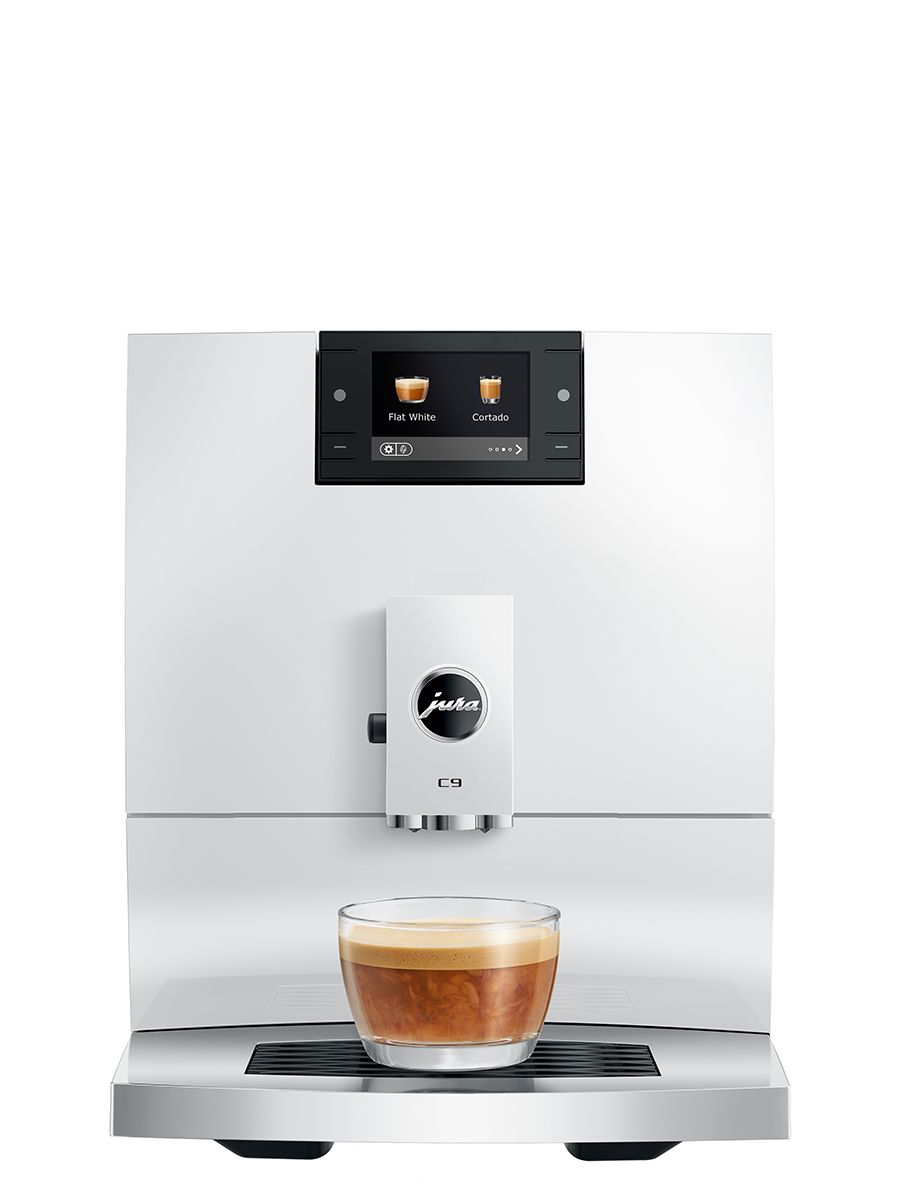 Front view of the JURA C9 Piano White automatic coffee machine dispensing coffee into a clear glass cup on the drip tray, with the display showing beverage options.